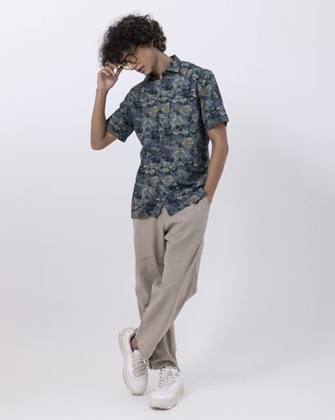 Trendy men's jungle print half-sleeve shirt paired with beige trousers and white sneakers, perfect for casual outings.