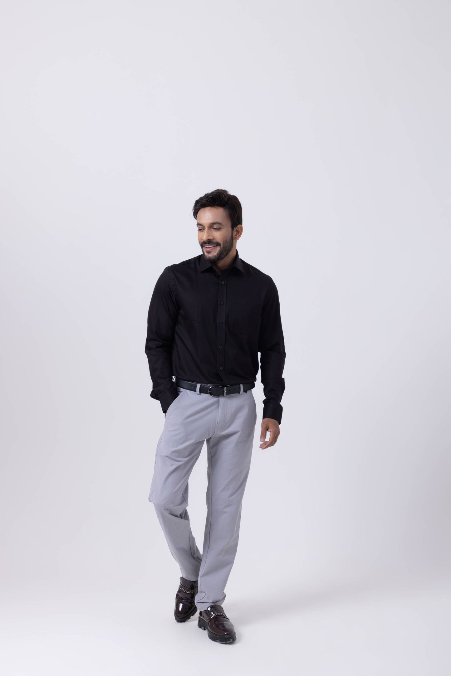 Man in black regular fit Giza cotton shirt and grey trousers, walking confidently.